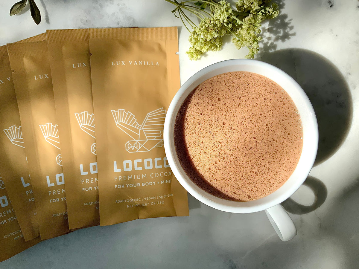 LOCOCO Lux Vanilla to-go cocoa sachets beside a cup of cocoa