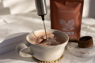 The LOCOCO frother whipping a cup of Original Spice cocoa, with the bag behind